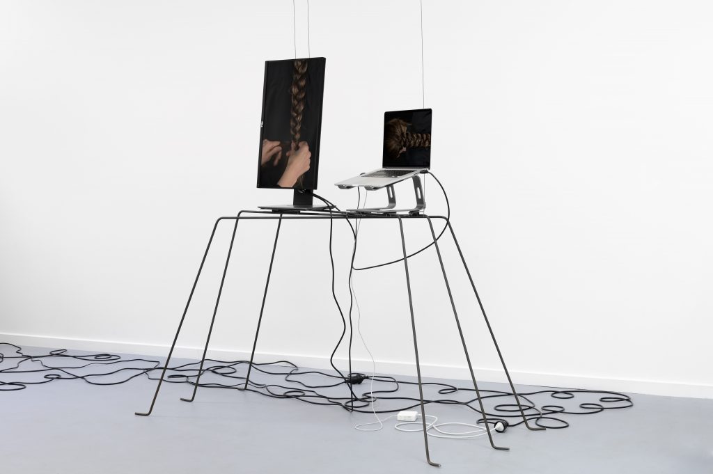 A laptop and a video monitor rest on a steel frame structure in a white room.