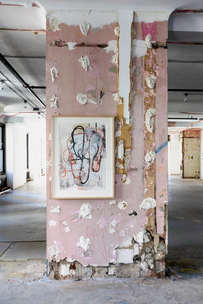 An artwork hangs on a pillar in a raw, vacant office space.