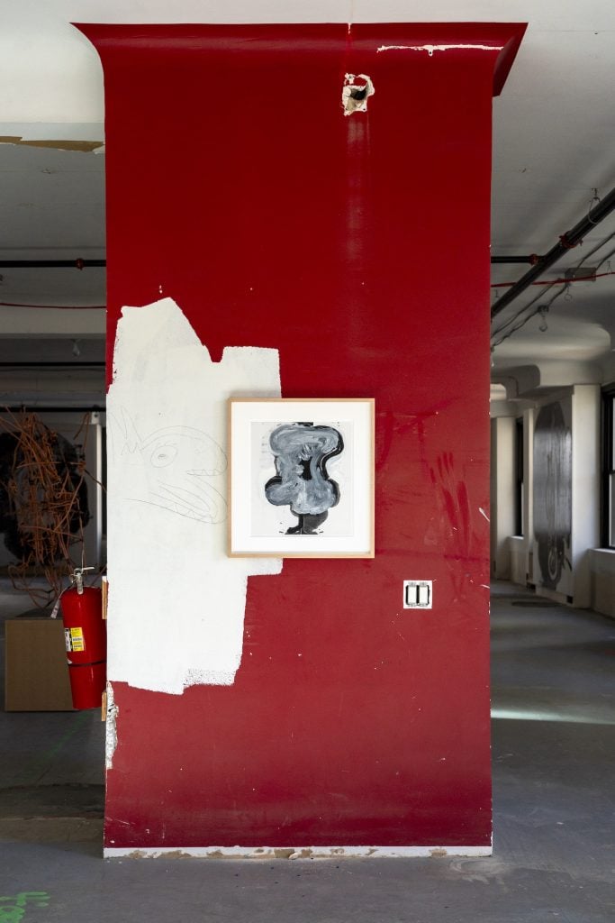 An artwork hangs on the side of a pillar painted burgundy in a raw, vacant office space.