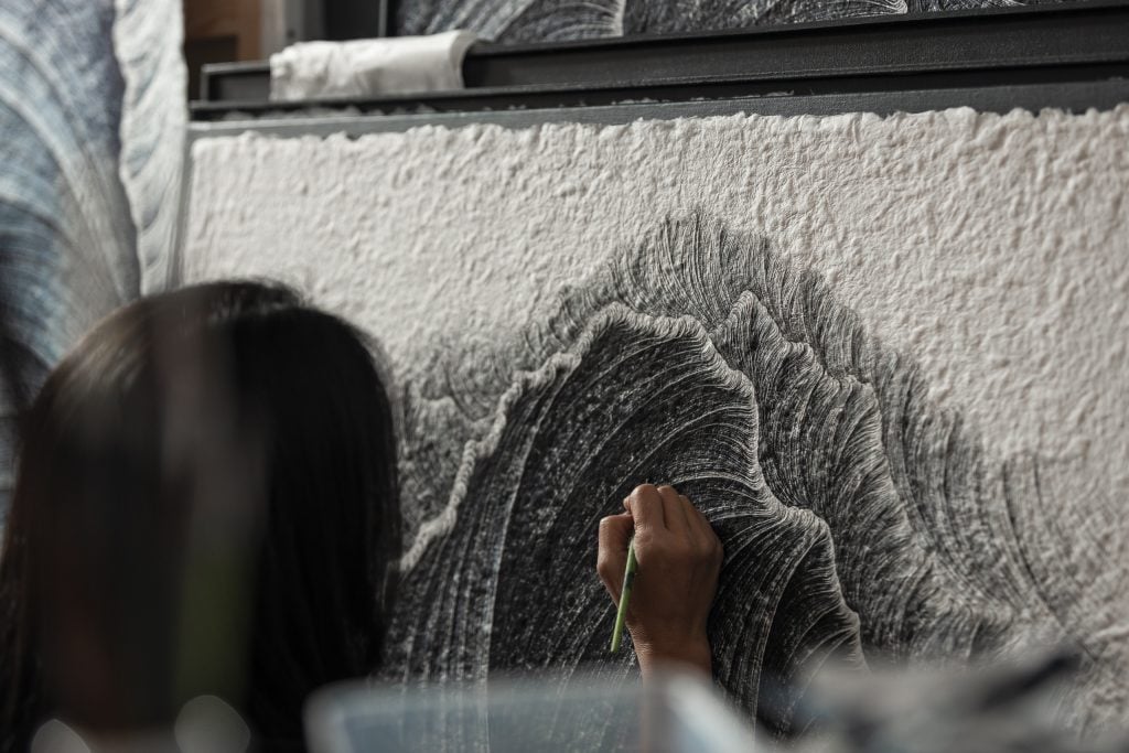 Closeup of the artist's head and hand working closely on applying ink to a new artwork in their studio.