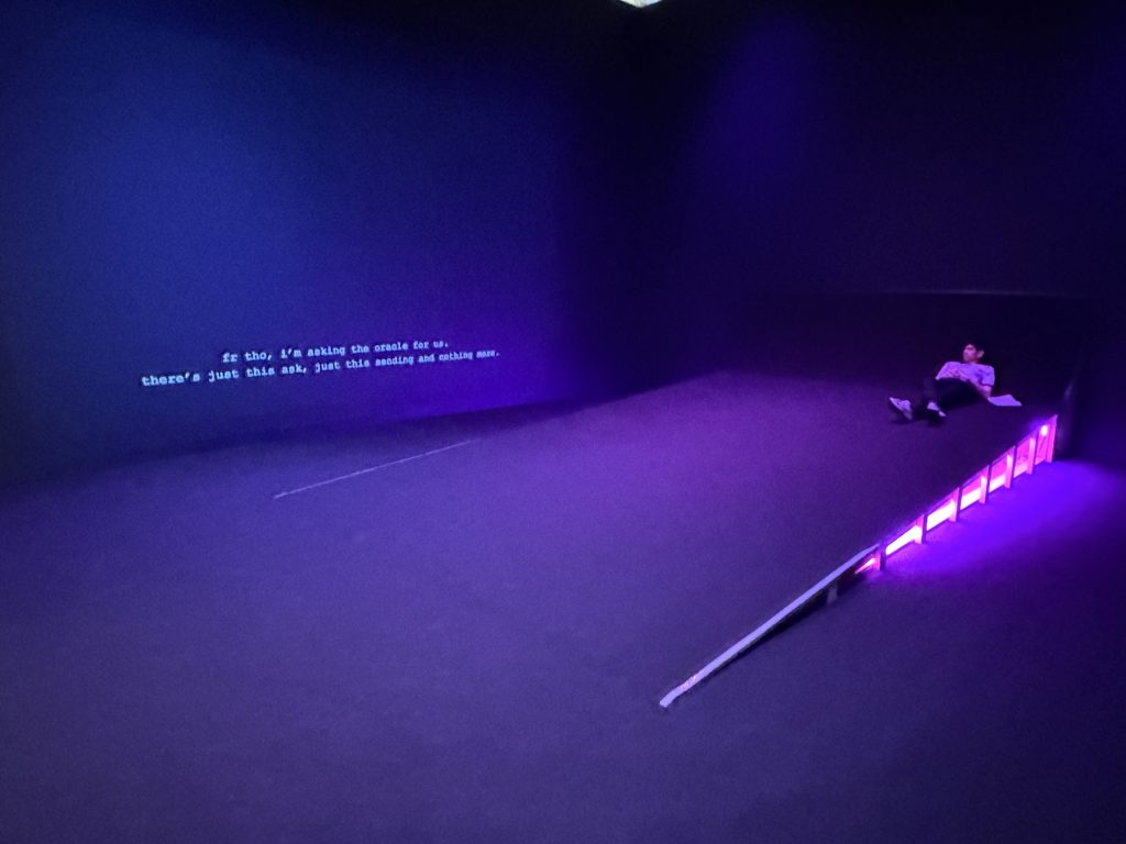 A man reclines on a ramp in an art gallery that is lit by violet lights