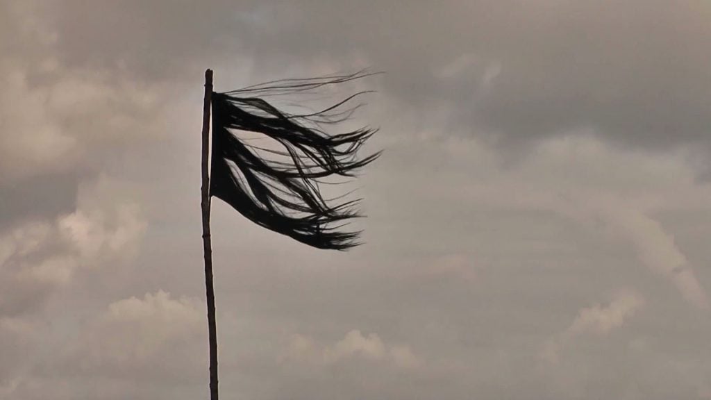 A threadbare black flag made from human hair stands against a cloudy sky.
