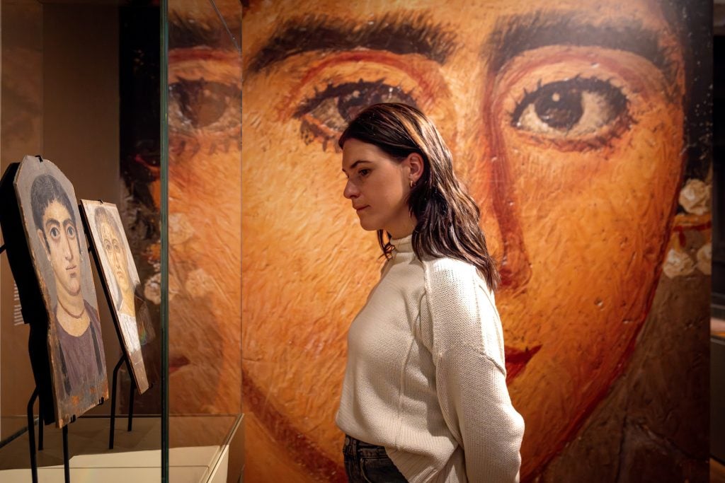 A woman viewing a display case with three ancient Egyptian portraits