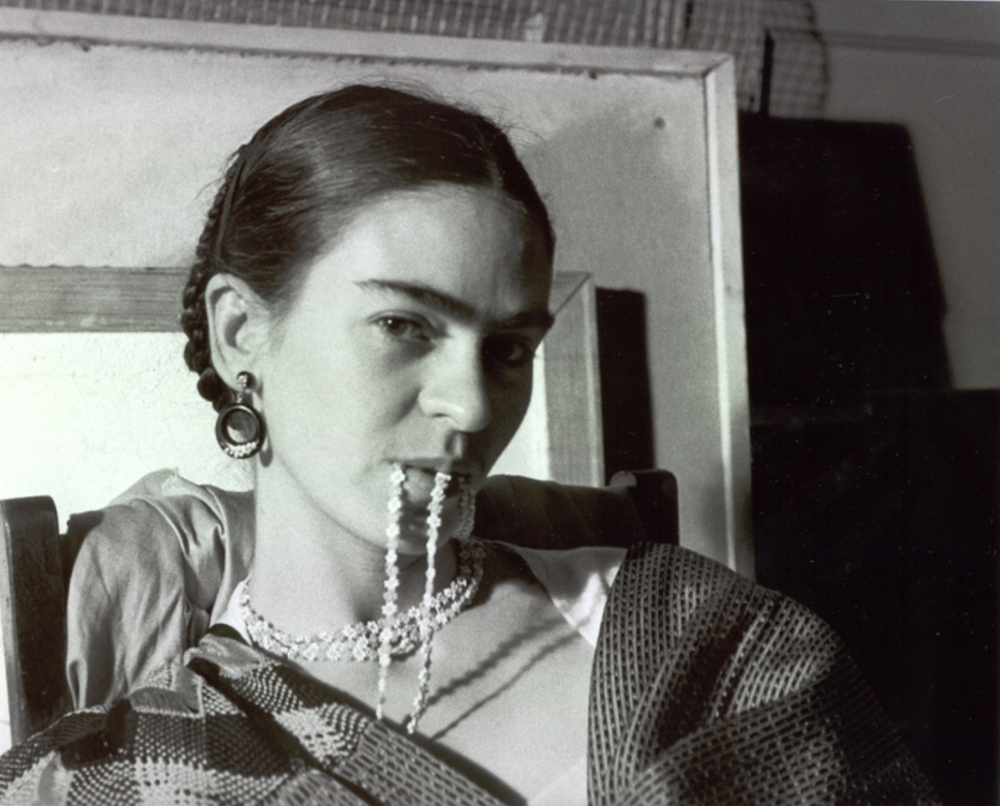 A portrait Mexican painter Frida Kahlo in Tehuana dress, holding a necklace in her mouth