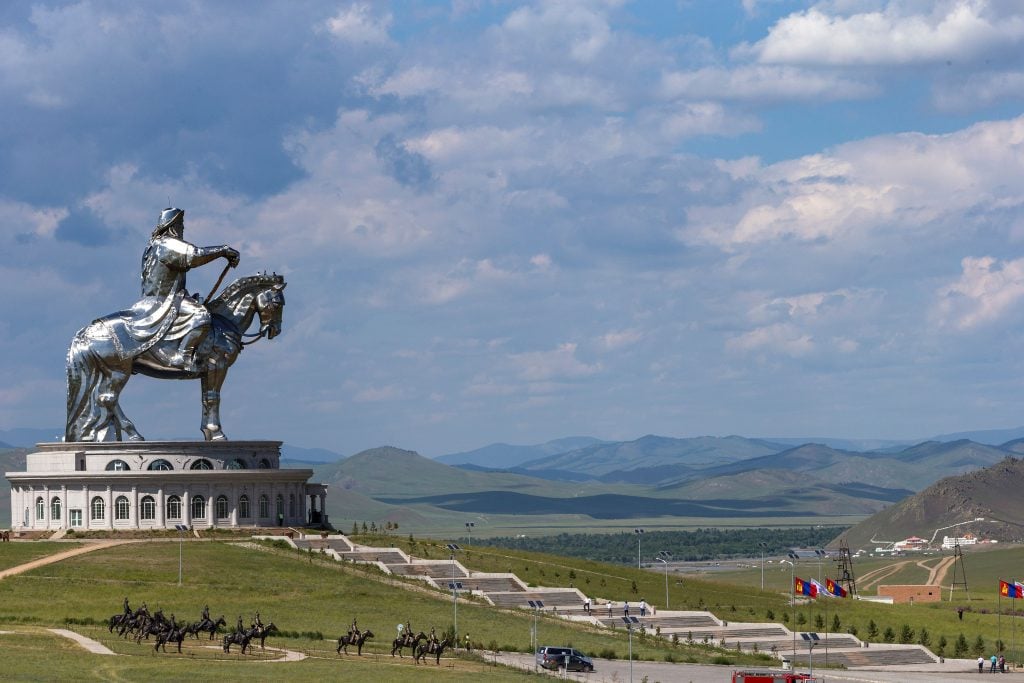 一尊银色的男子骑马雕像矗立在蓝天白云下的辽阔平原上。