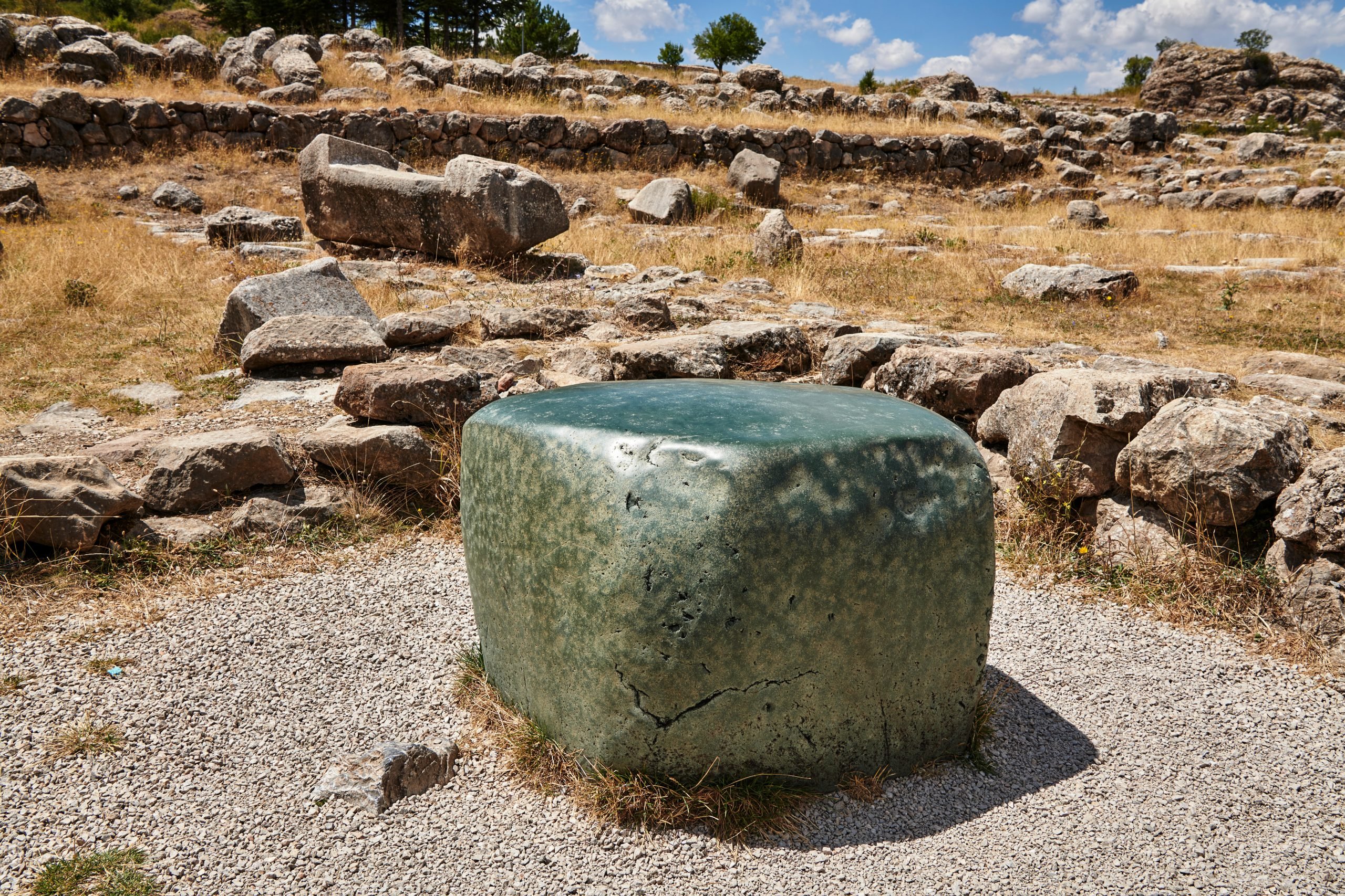 A large green stone surrounded by the remains of an ancient temple in Hattusa, Turkey