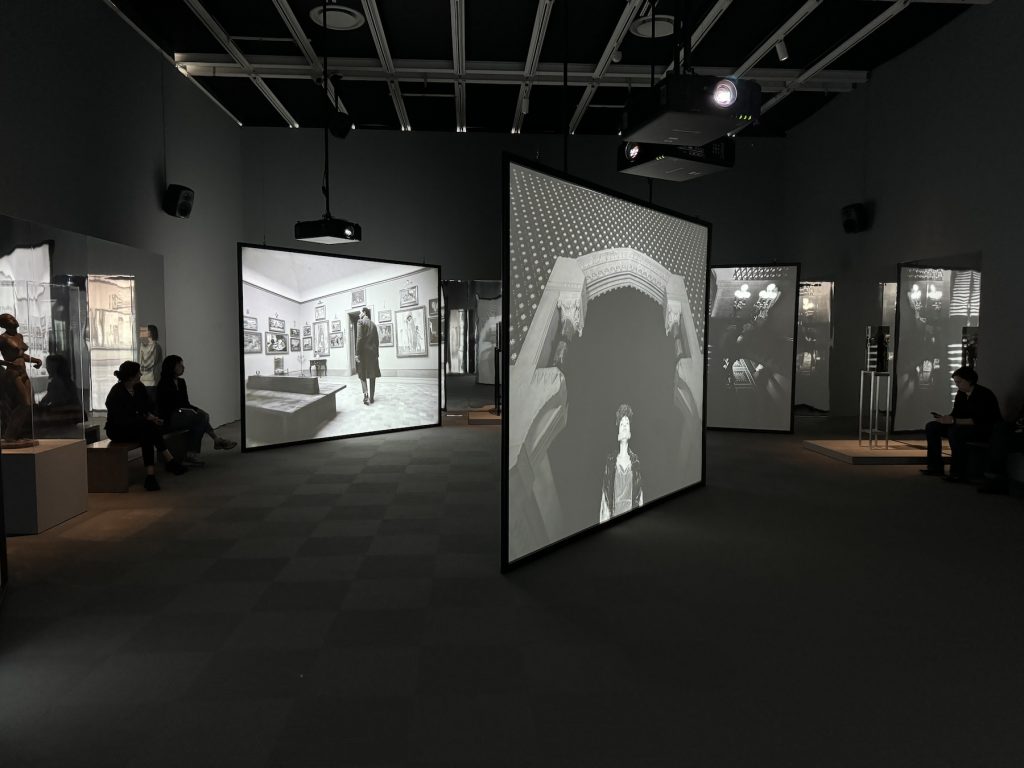 Multiple screens playing black and white footage in an art gallery
