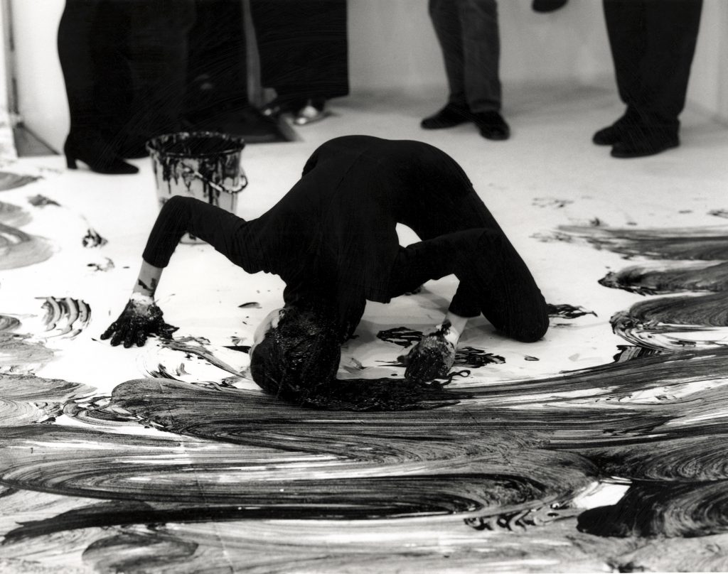A woman paints a floor black with her head, soaked in black hair dye.