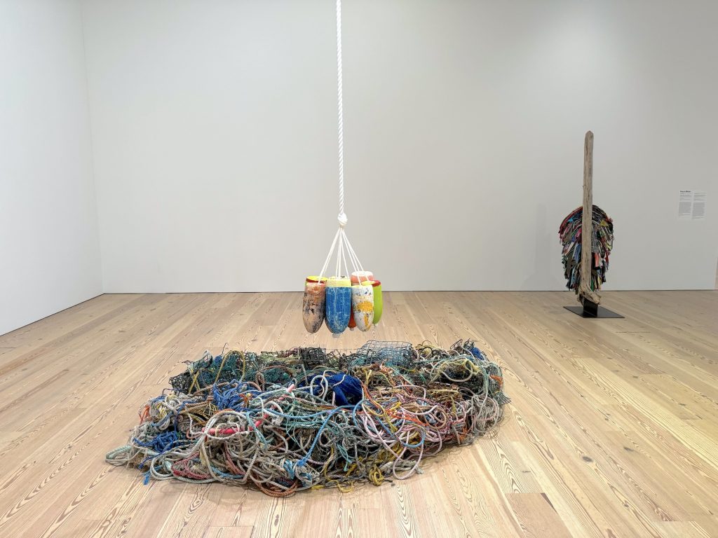 A sculpture made of hanging buoys and lobster traps next to a sculpture made of driftwood and worn clothing