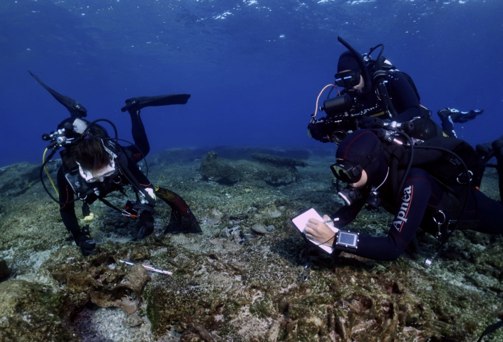 A photo of three underwater divers recording archaeological remains barely buried under the sea floor