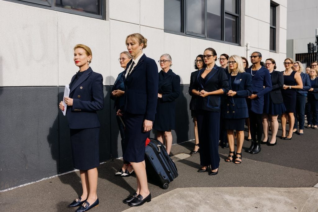 A group of women, led by artist Kirscha Kaechele, in matching blue business suits.
