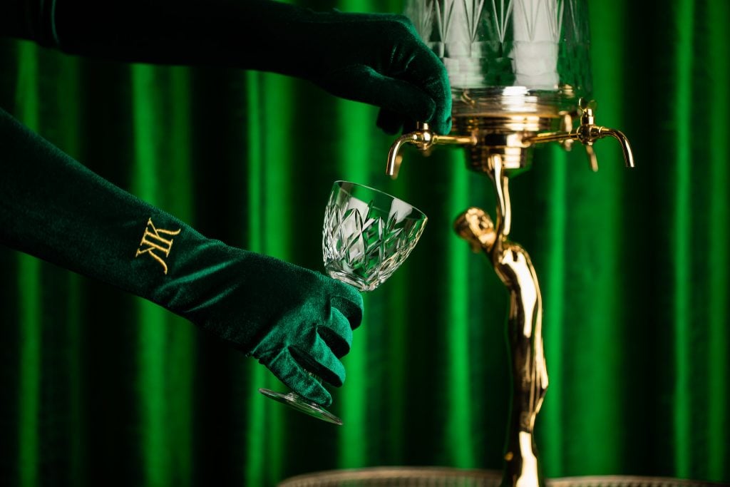 A pair of hands in green gloves pulls a draft drink against a lush green background.