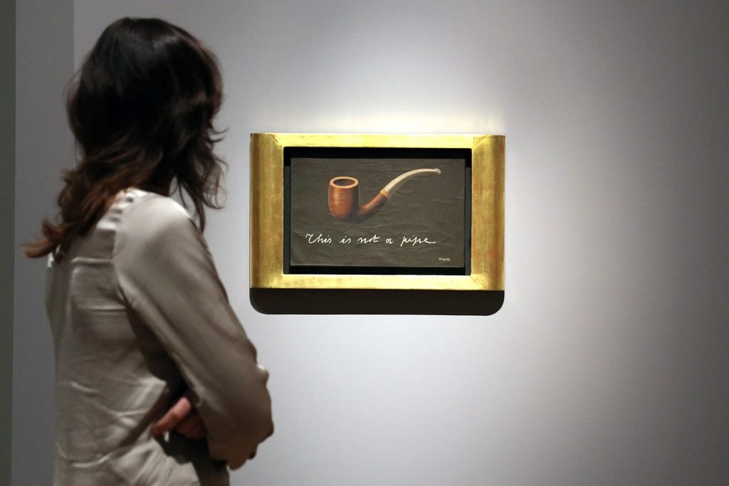 A woman looks at a Rene Magritte painting of a pipe with the caption 
