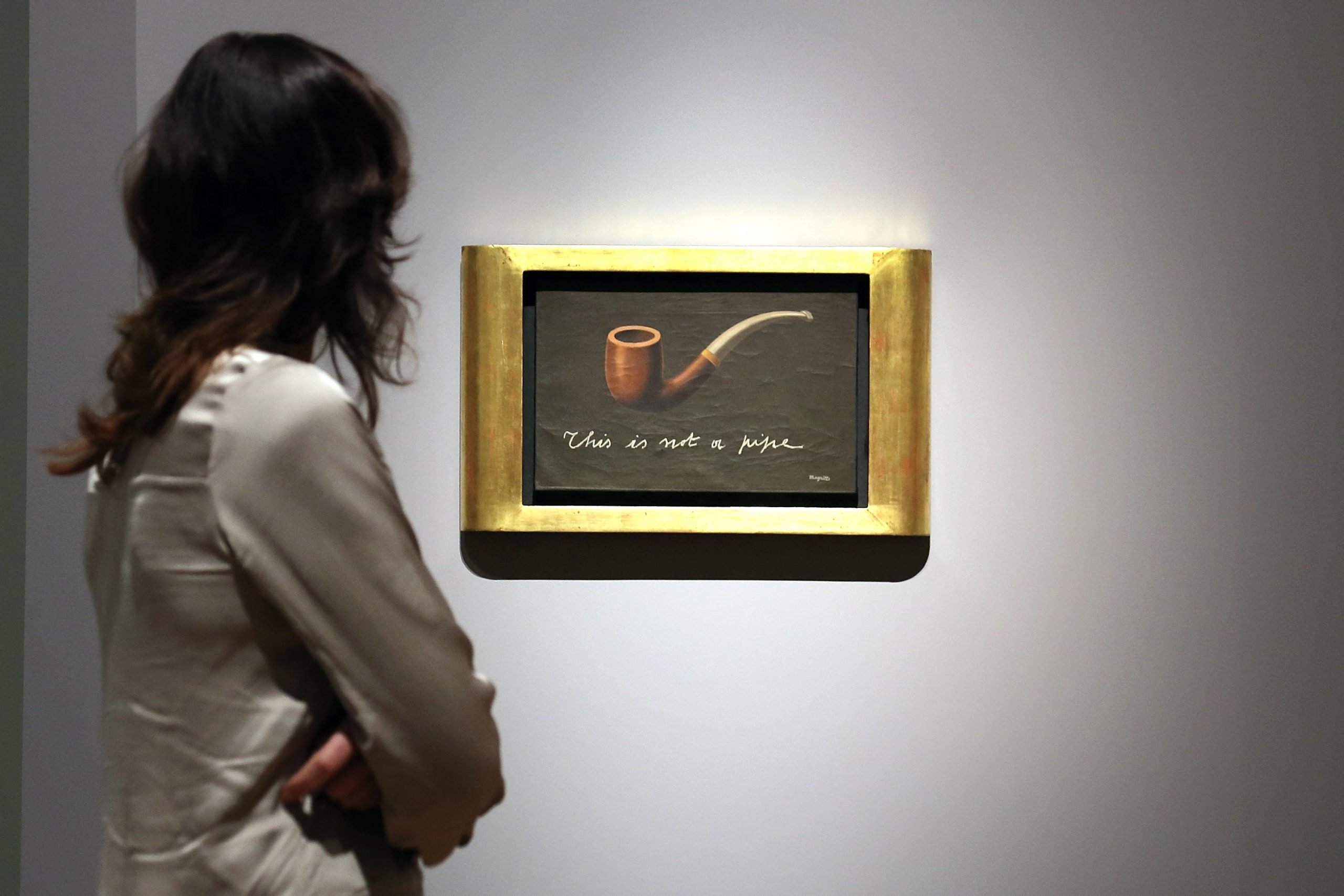 A woman looks at a Rene Magritte painting of a pipe with the caption "This is a not a pipe."