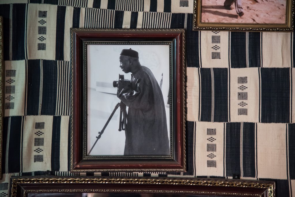 A framed photo of the Malian photographer Malick Sidibé, seen against a backdrop of African textiles at his photo studio.