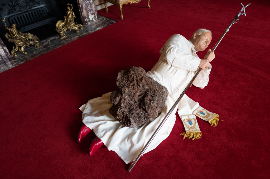 photograph of a sculpture in the form of pope john paul ii being hit by a meteorite.