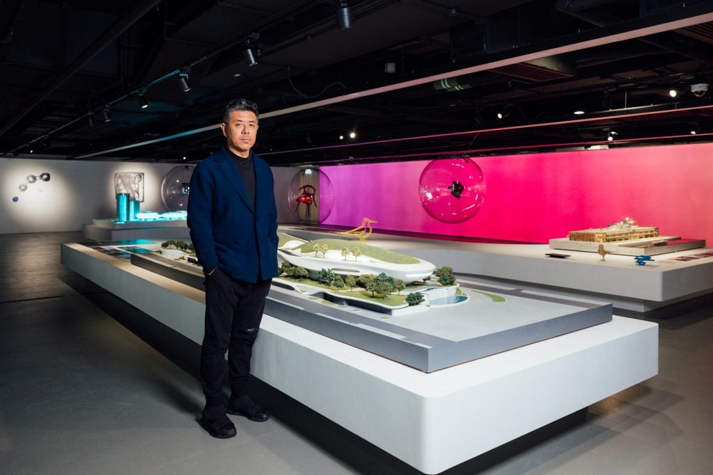 Architect Ma Yansong stands in front of one of the display cases in a black suit at his exhibition at HKDI gallery in Hong Kong.