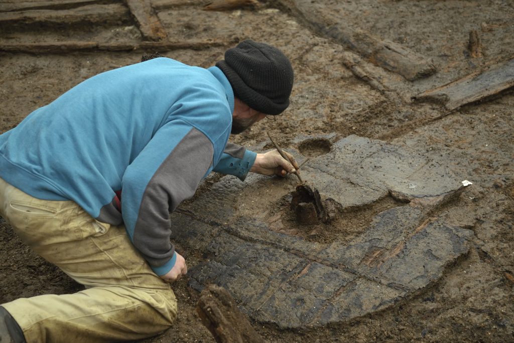 An archaeologist excavating a wooden plank.
