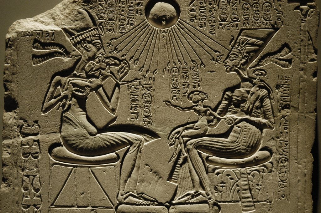 A rock relief depicting a man and woman sitting and facing each other, with a sun's rays beaming down on them.