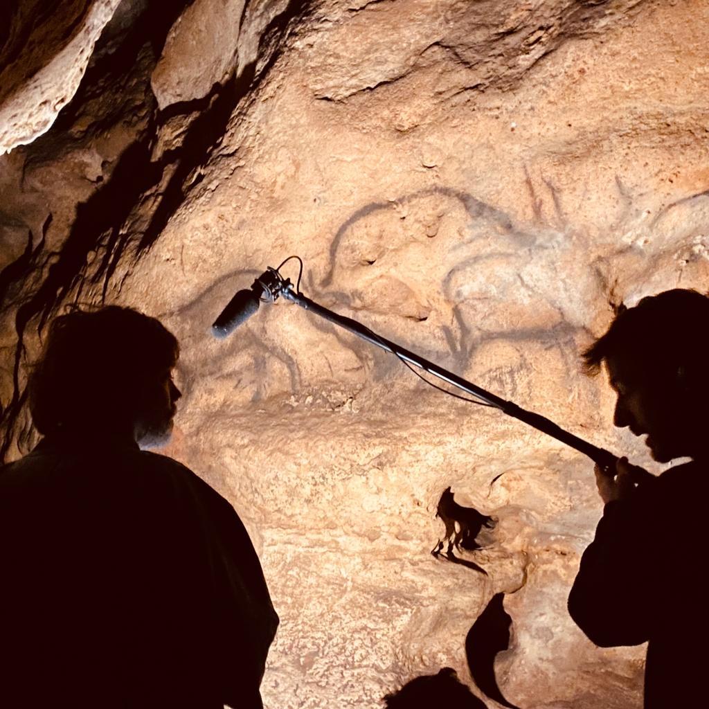 Oliver Beer and Rufus Wainwright with recording equipment in a cave with wall paintings.