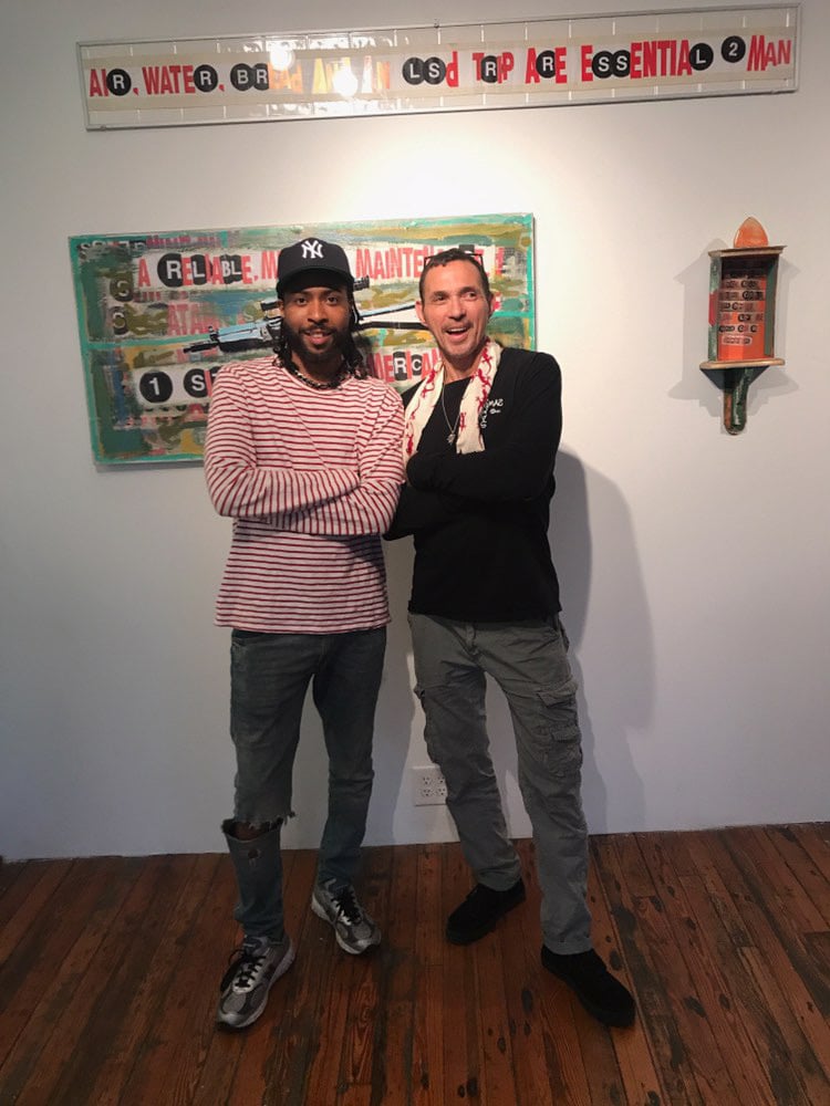 A photograph of two smiling men standing before graffiti-inspired artworks at an exhibition