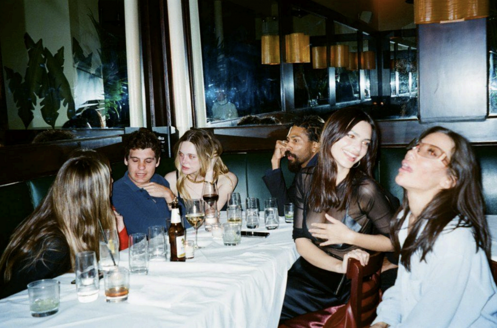 A picture of six people seated and partying around a white table littered with wine glasses in a dark, fashionable restaurant