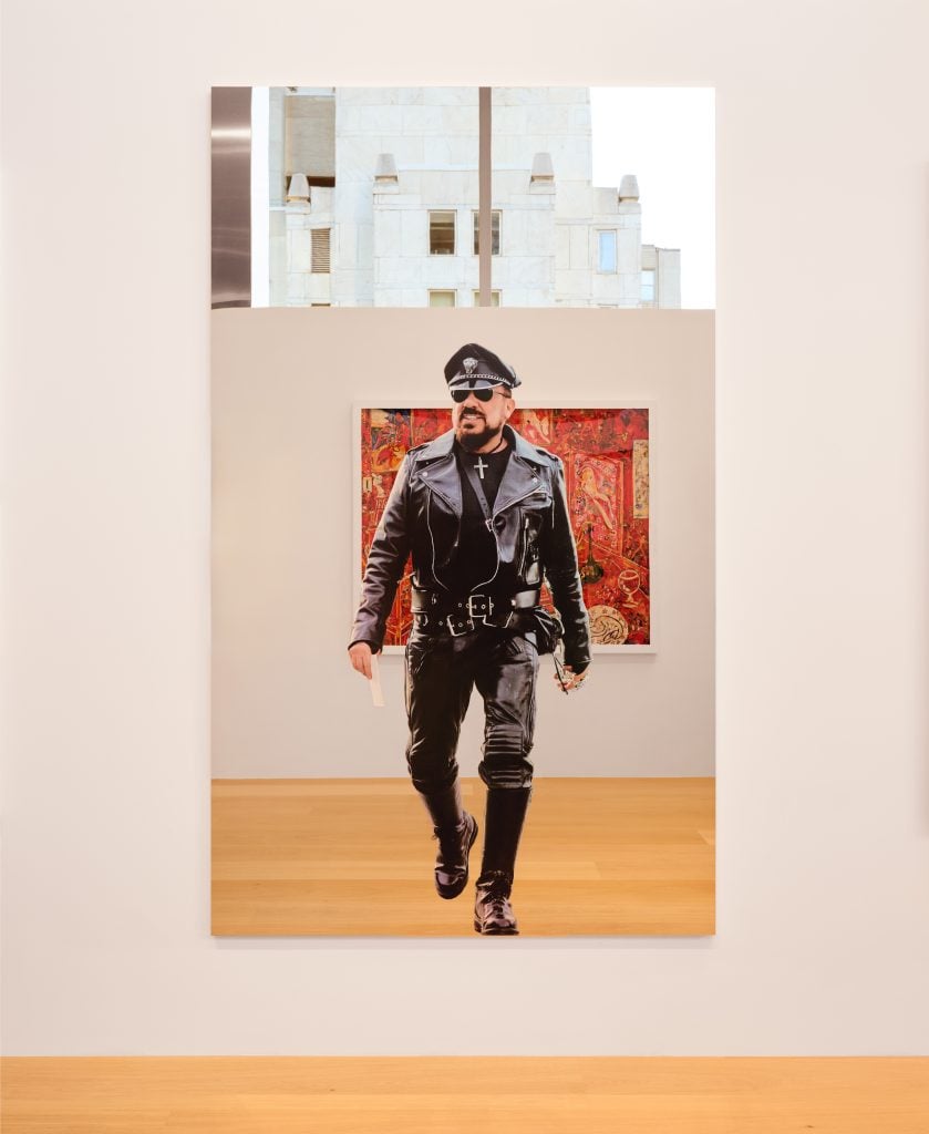 A mirror depicts the image of a man in full leather regalia and sunglasses 