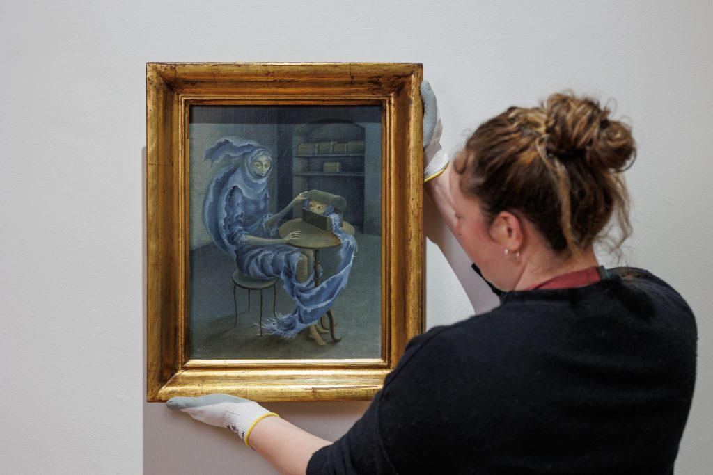 A woman hangs a painting by Surrealist artist Remedios Varo.