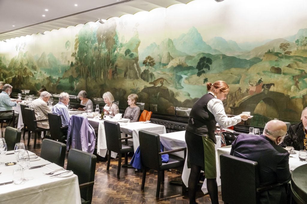 people dine at tables in front of a large painted mural in a museum, identified as Tate Britain