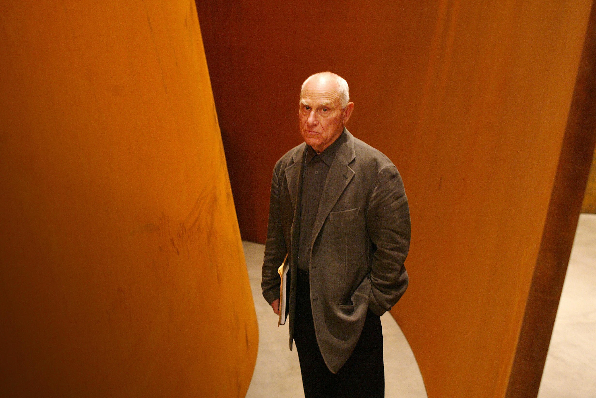 a man stares out at the camera with large steel sheets erected behind him.