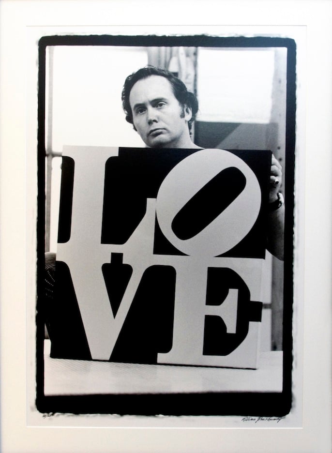 Artist Robert Indiana poses with a painting of the word "Love."