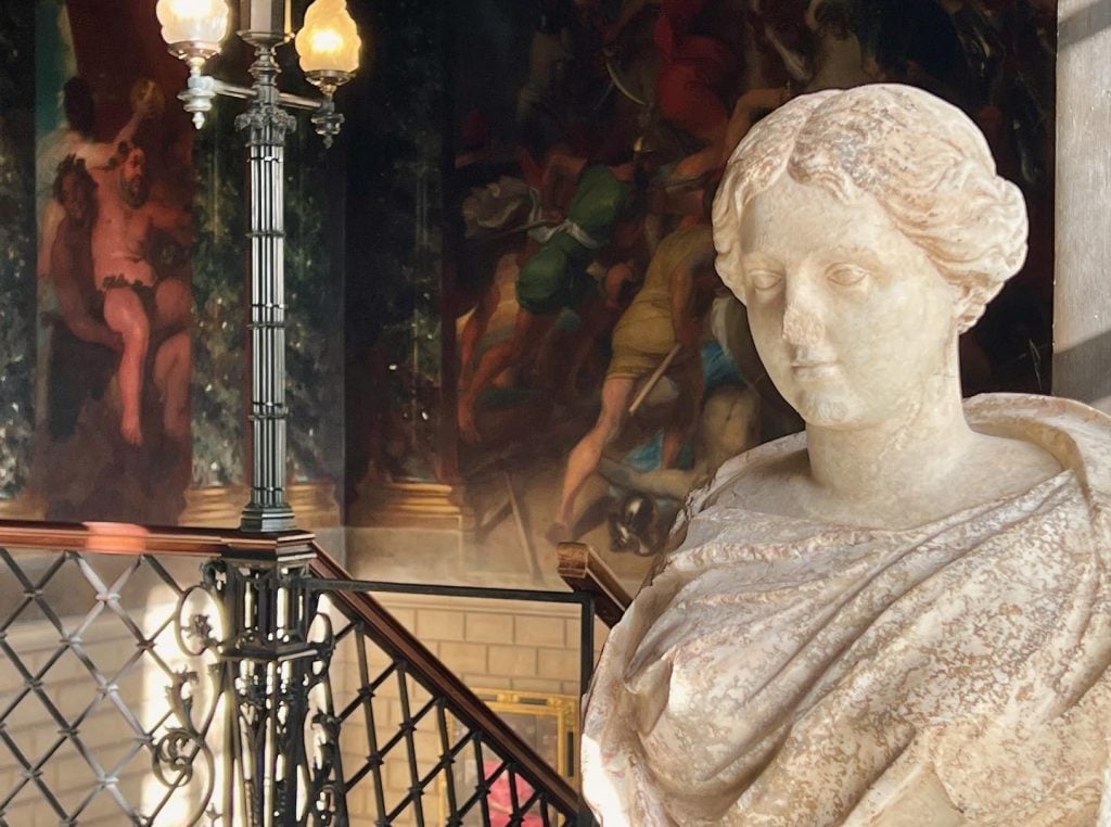 A Roman bust next to a grand staircase.