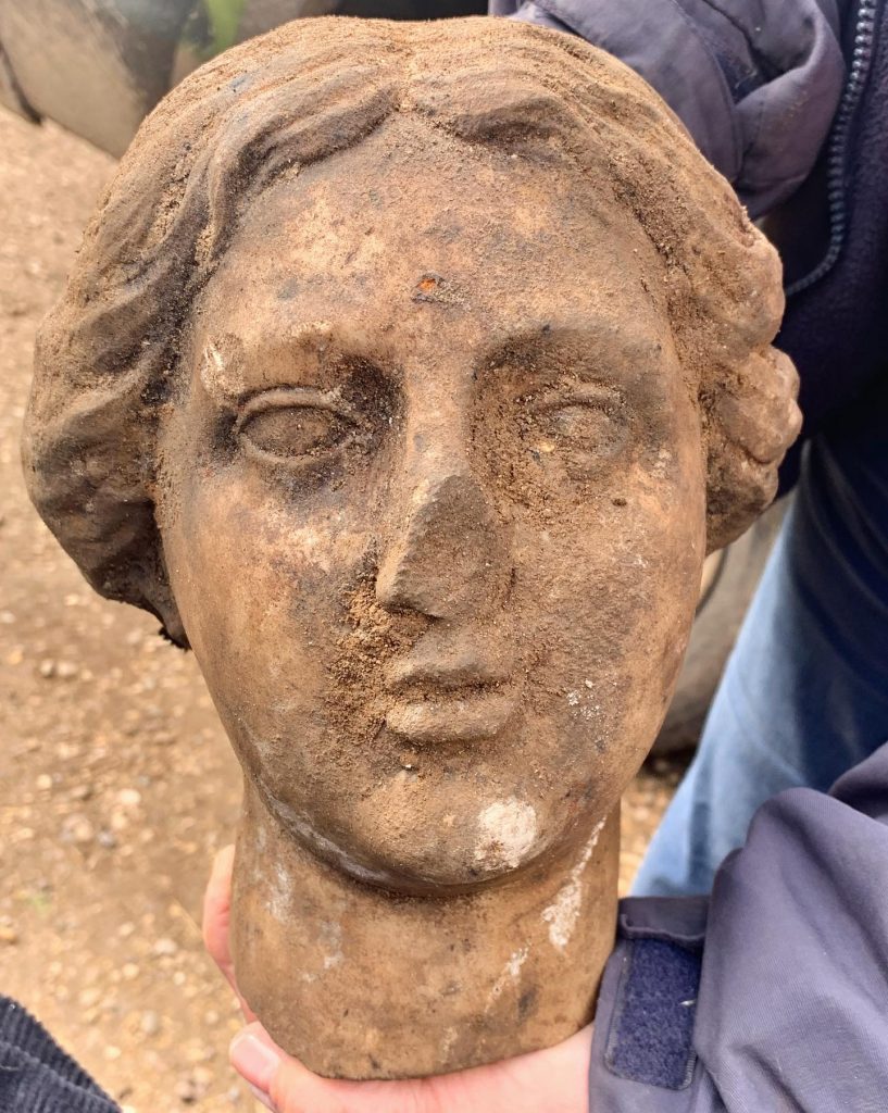 A Roman bust covered in dirt, its nose broken off.