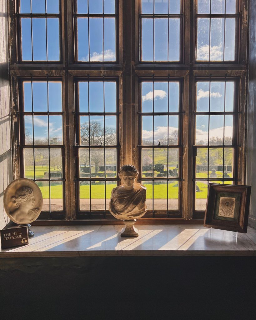 A Roman bust displayed in front of a large window that looks out on a blue sky and a graveyard.