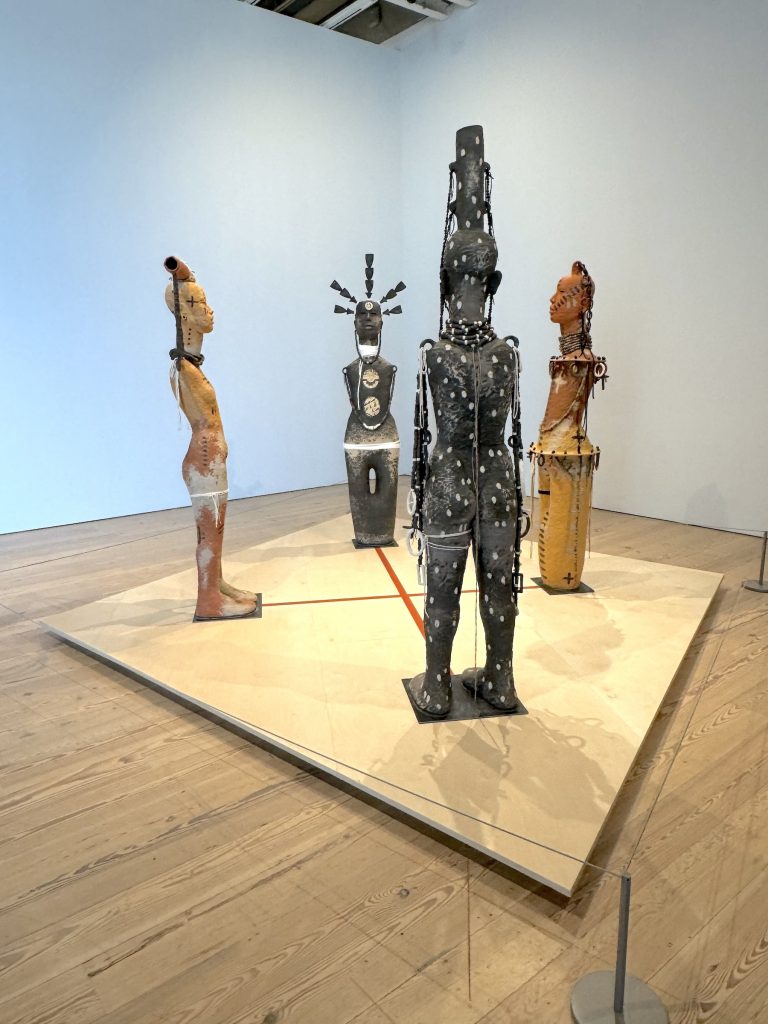 Four ceramic female figures facing each other on a low platform in a gallery
