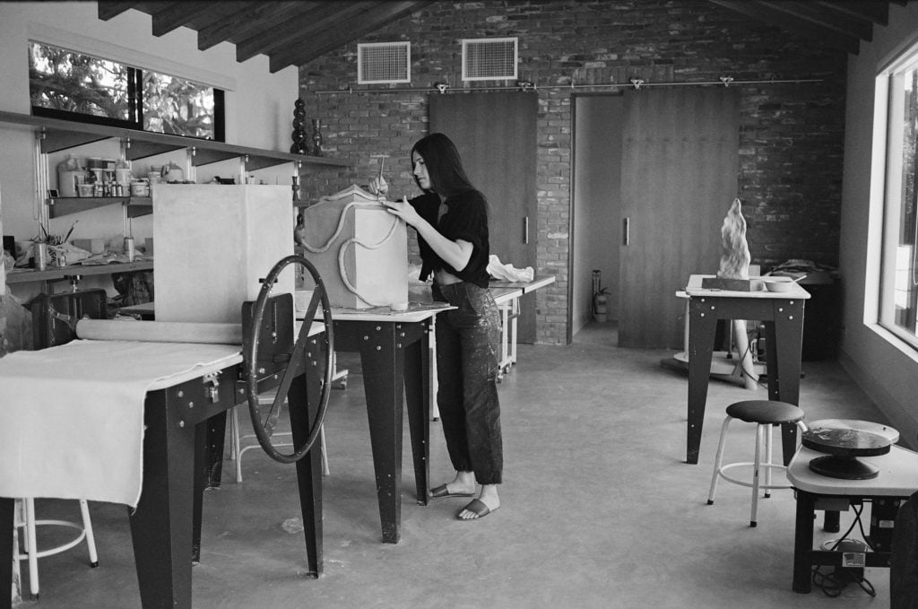 a black and white photo of a young woman who is the artist Sachi Moskowitz in her ceramics studio