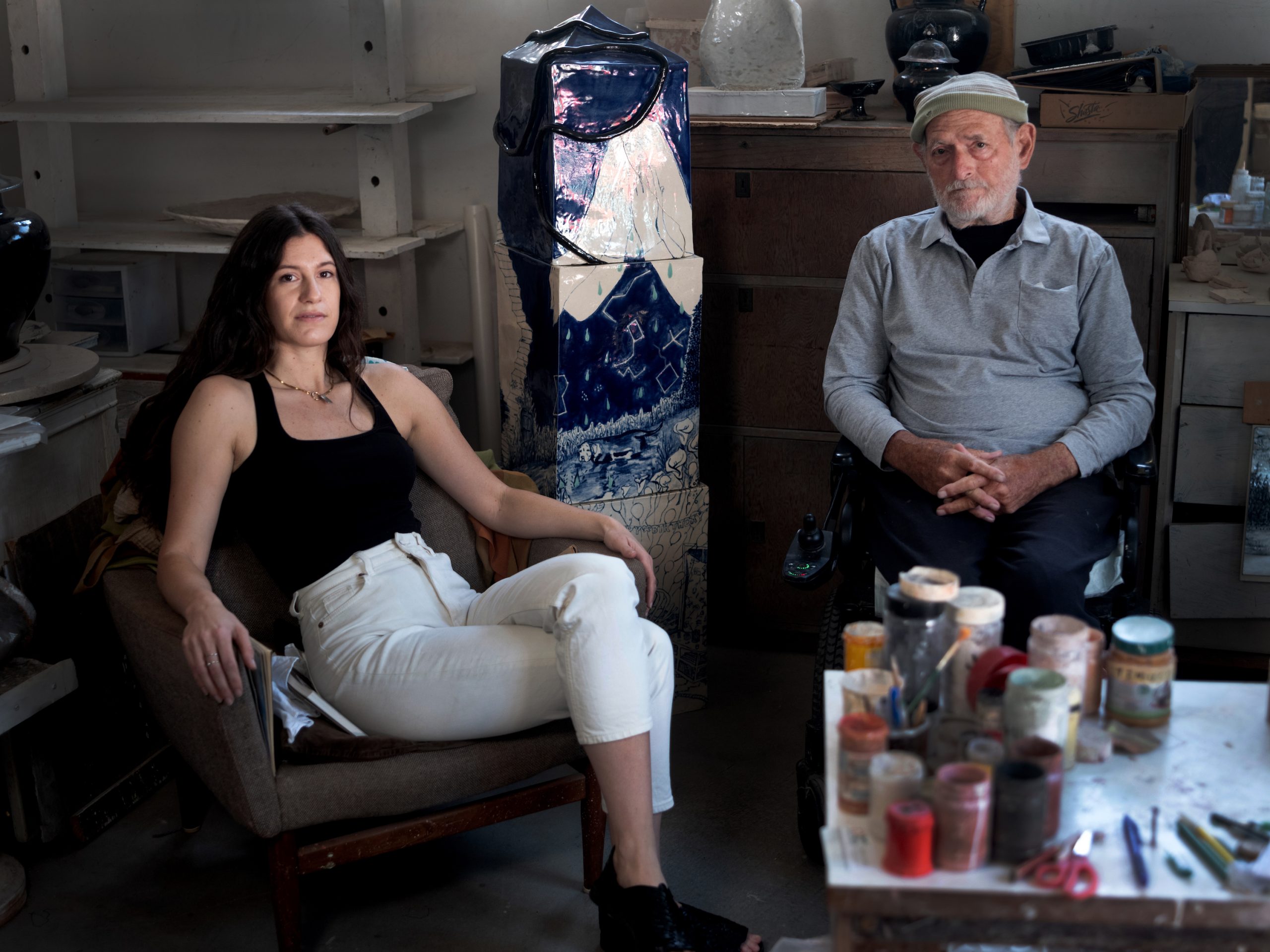 a young woman seated wearing a black shirt and white pants, and a older man also seated wearing a shirt and paperboy hate