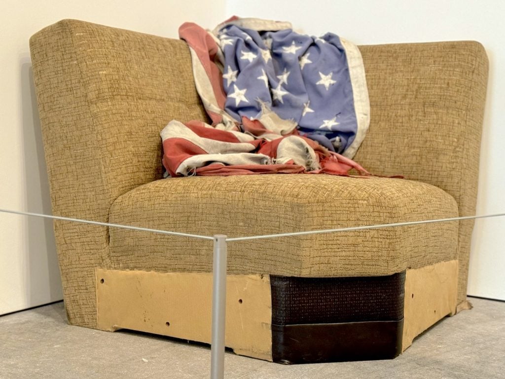 A dingy piece of a sectional couch with a crumpled American flag on it