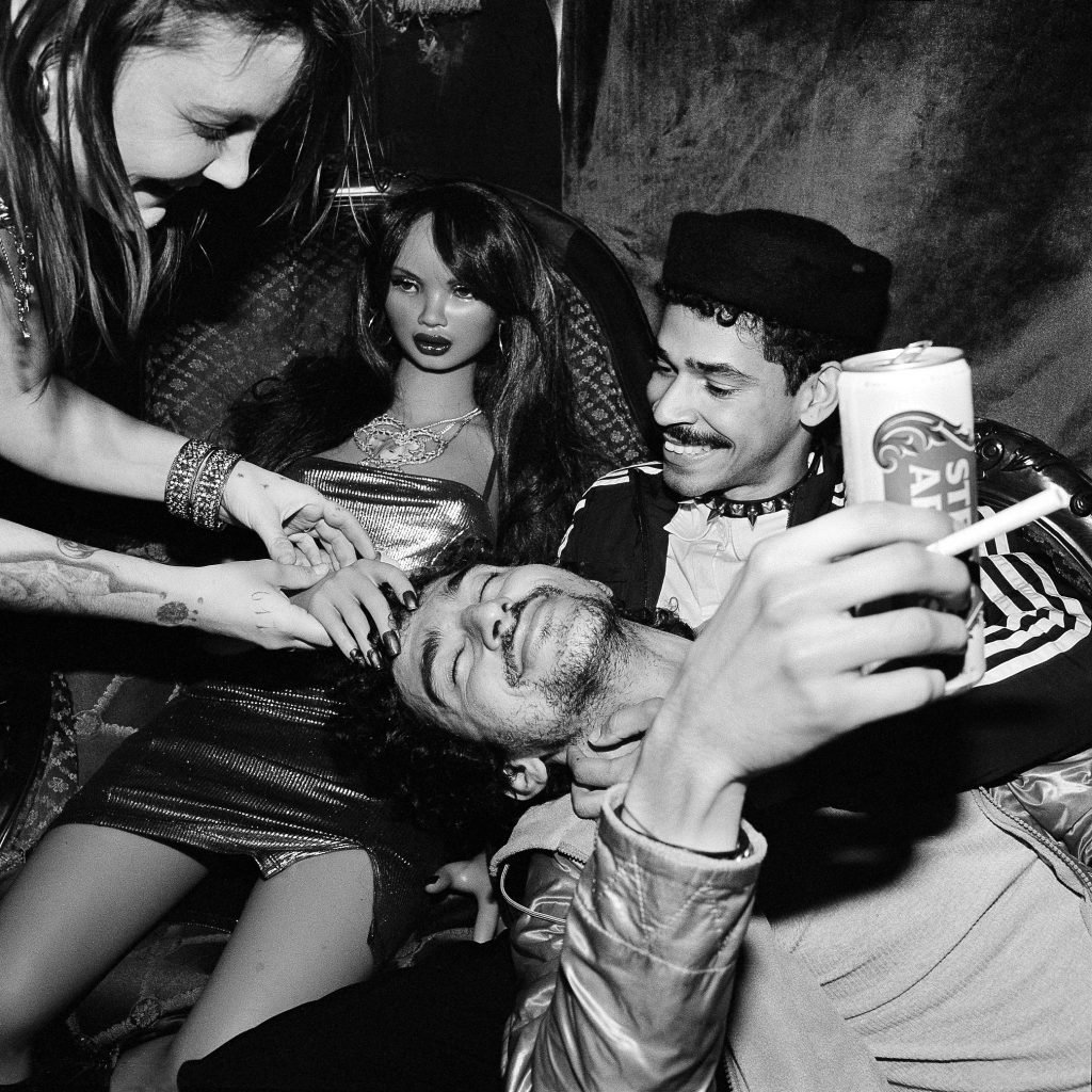 A black and white Polaroid of four young artists piled atop each other while partying, includig the doll Skye Cleary