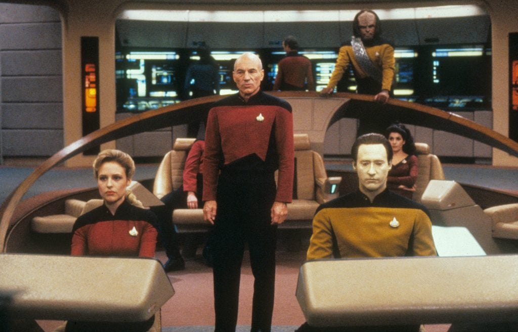 Two men and a woman, dressed in uniforms, seated in a spaceship set from the Star Trek TV series.