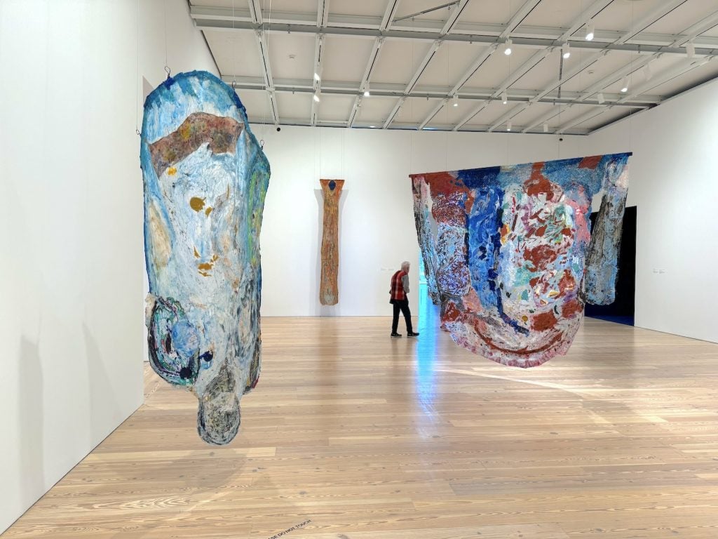 A gallery full of irregularly shaped hanging abstract paintings