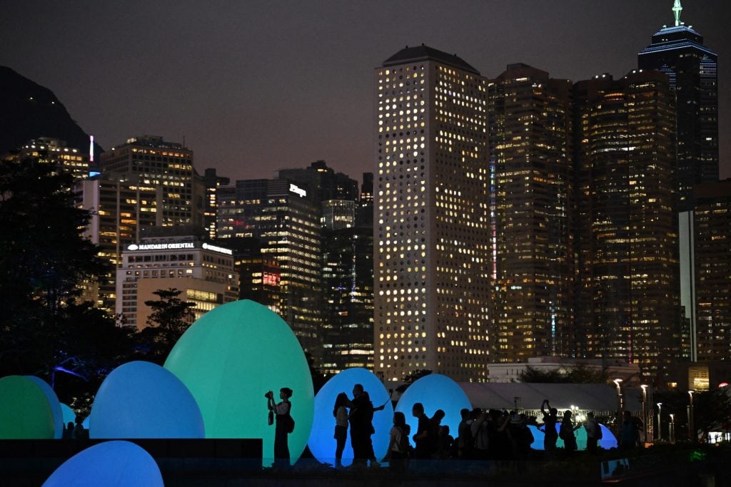 a crowd gathers in front of gigantic egg-shaped installation in front of the Hong Kong skyline