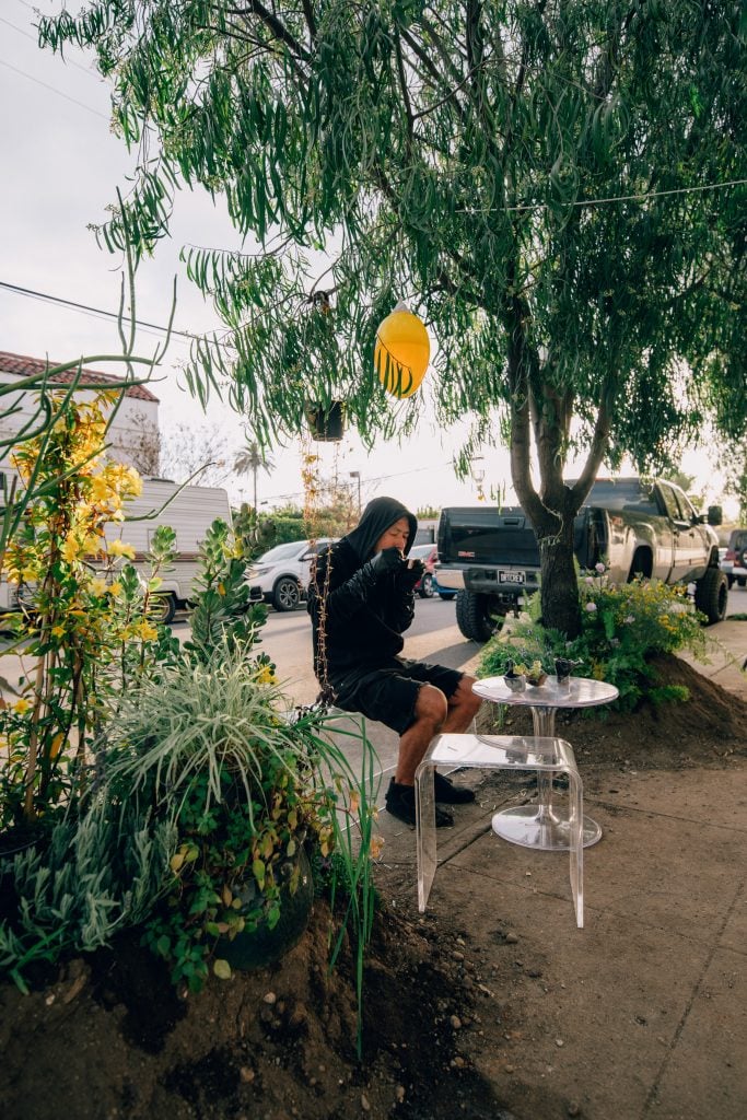 Artist Terence Koh sitting outside between trees in Los Angeles