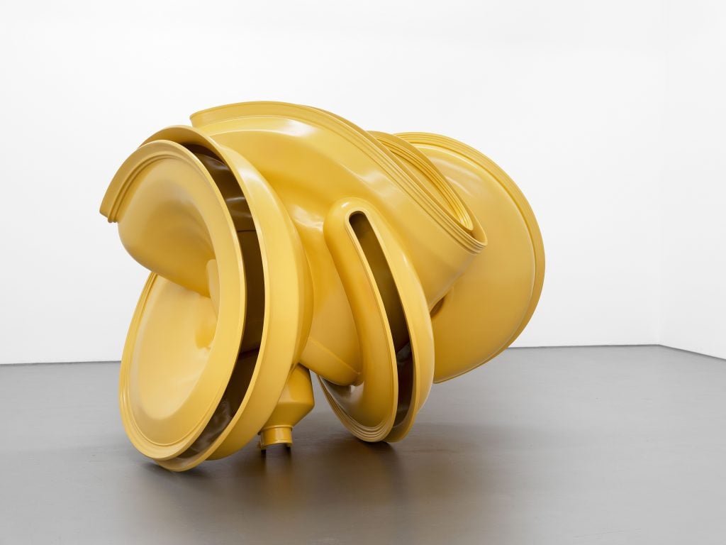 A large-scale abstract yellow sculpture in a white gallery space.