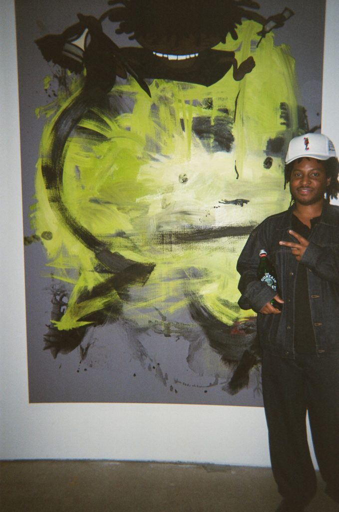 a man stands in front of an abstract painting of bright yellow and black.