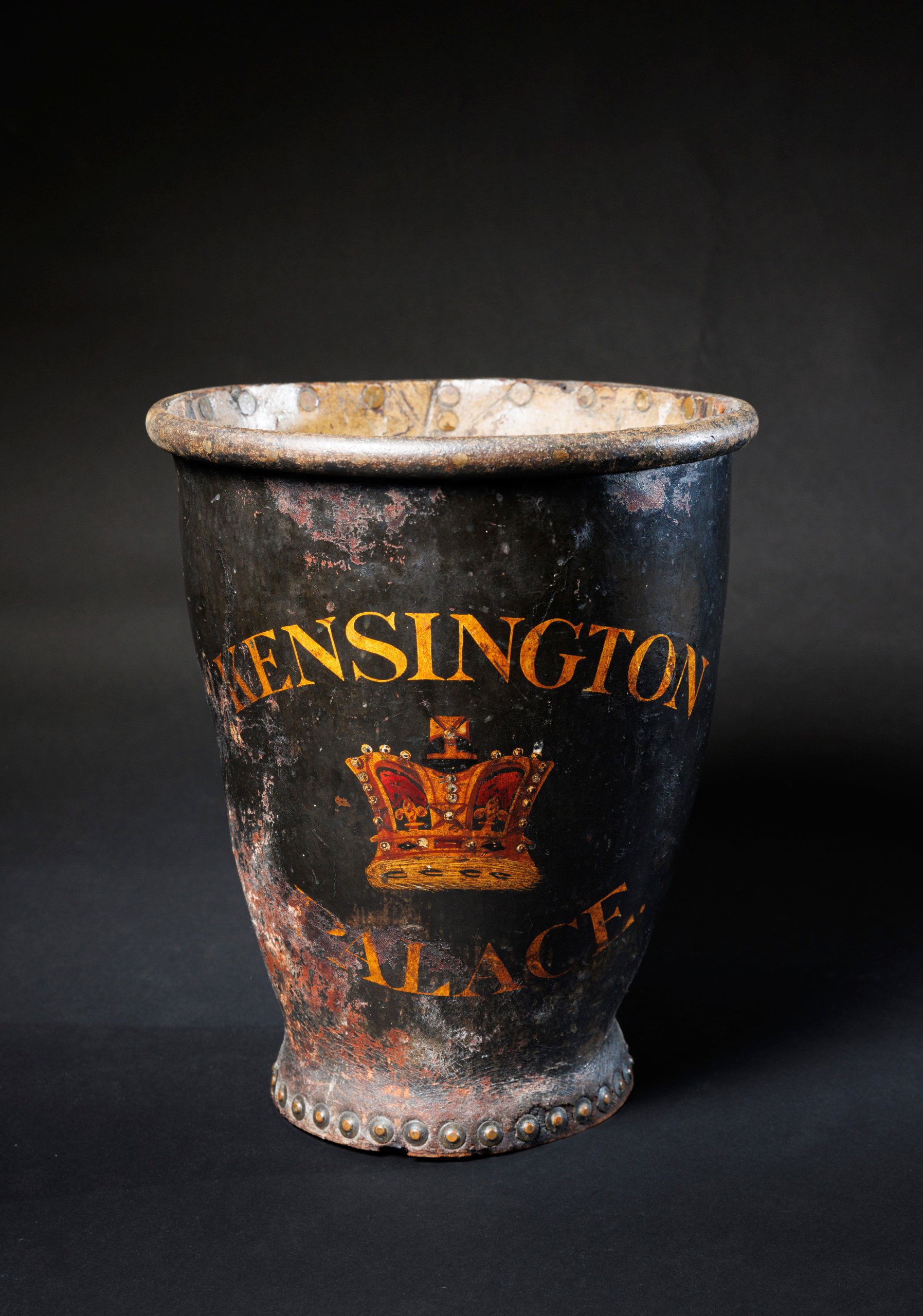 Photograph of a worn black leather fire bucket embalzoned in bronze with 'Kensington Palace' and a crown between those two words