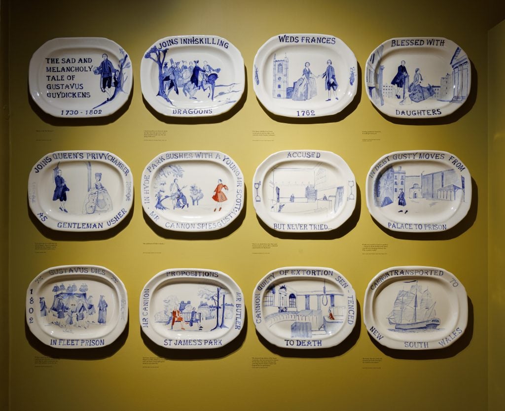 A photograph of 12 narrative ceramic plates on a yellow wall