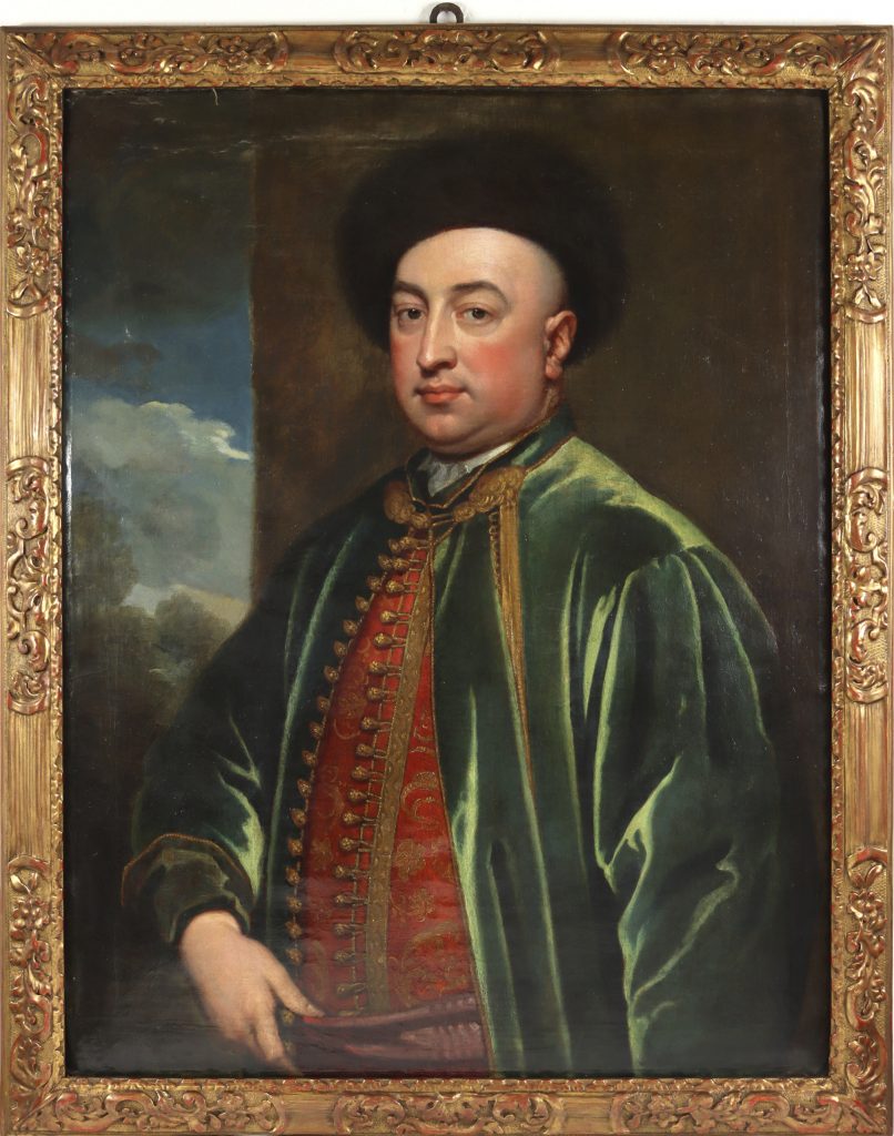Photograph of a gold-framed portrait depicting a fair-skinned man wearing a velety green coat, red vest, and black hat