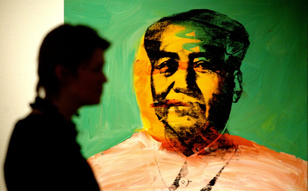 A man walking past Andy Warhol's screen print of Chairman Mao.