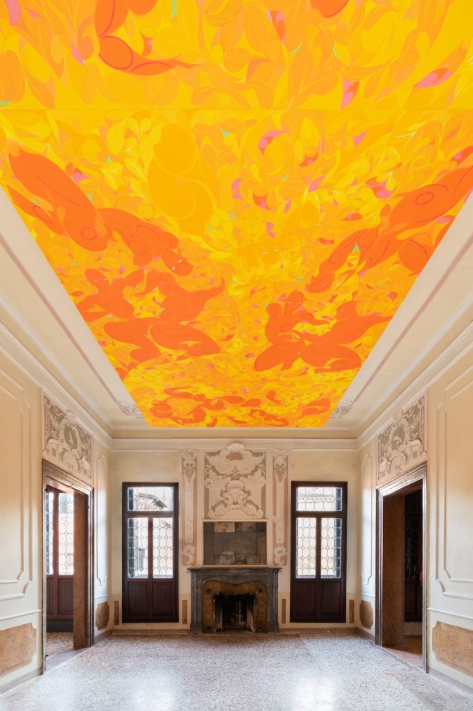 A bright yellow and orange painting on the ceiling of an ornately decorated room with cream walls and a grand fireplace.